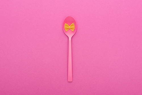 uncooked farfalle pasta on plastic spoon bowl isolated on pink