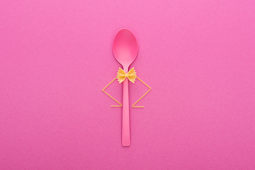 uncooked farfalle pasta on plastic spoon and spaghetti isolated on pink