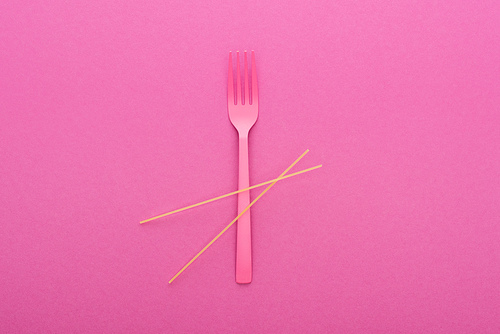 top view of pink plastic fork and spaghetti isolated on pink