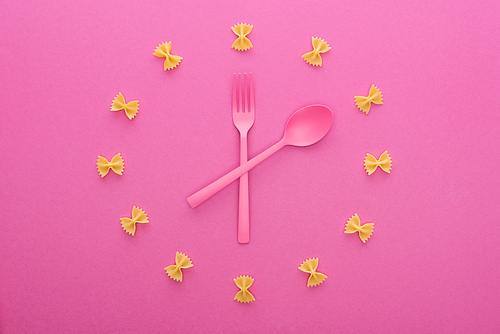 top view of clock concept with uncooked farfalle pasta, plastic fork and spoon in middle isolated on pink