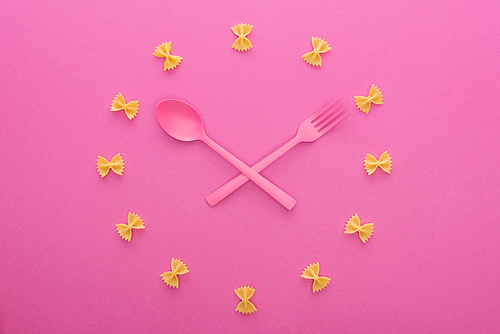 clock concept with crossed pink plastic fork and spoon isolated on pink