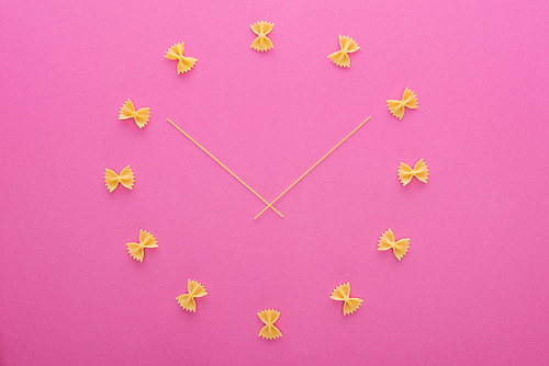 top view of clock concept with uncooked farfalle pasta and spaghetti in middle isolated on pink