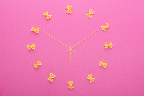 top view of clock concept with uncooked farfalle pasta and spaghetti isolated on pink
