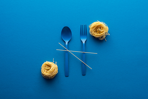 top view of blue plastic spoon and fork with spaghetti  near vermicelli pasta on blue background