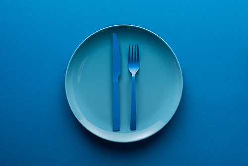 blue plastic knife and fork on plate on blue background