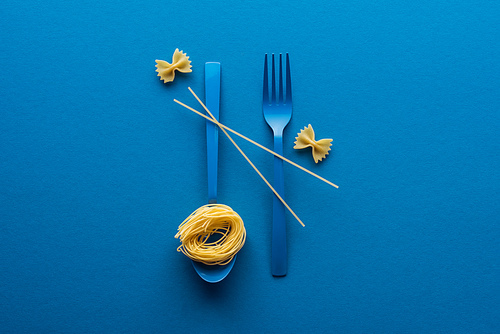 vermicelli pasta on blue plastic spoon with spaghetti on fork and spoon near farfalle pasta on blue background