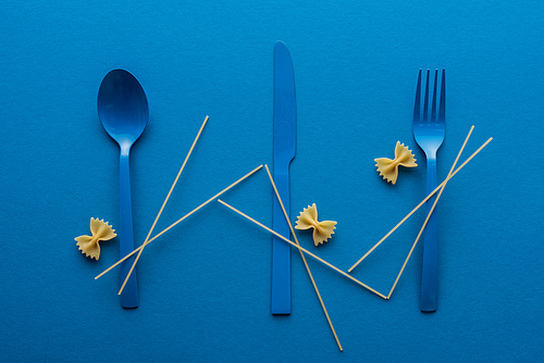 blue plastic cutlery with spaghetti and farfalle pasta on blue background