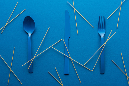 blue plastic cutlery with uncooked spaghetti around on blue background
