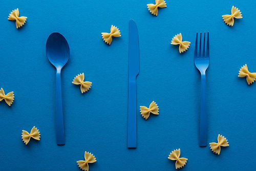 blue plastic cutlery with uncooked farfalle pasta around on blue background