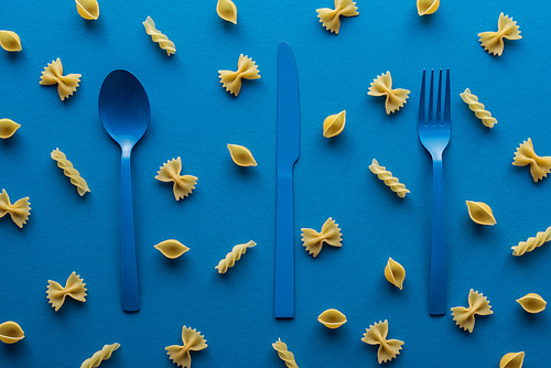 blue plastic cutlery with uncooked pasta around on blue background