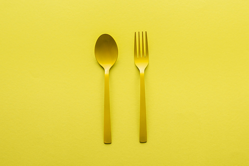 top view of yellow spoon and fork isolated on yellow