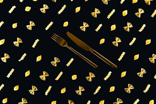 flat lay of different kinds of pasta with metal cutlery in middle isolated on black