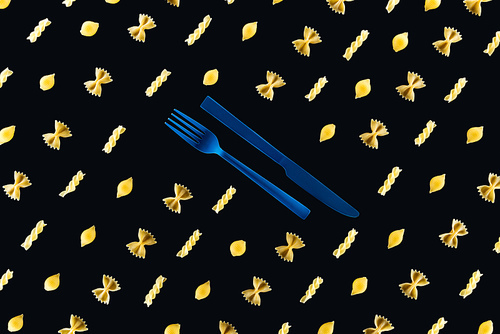 flat lay of different kinds of pasta with plastic blue fork and knife in middle isolated on black