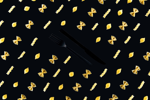 flat lay of different kinds of pasta with plastic black fork and knife in middle isolated on black