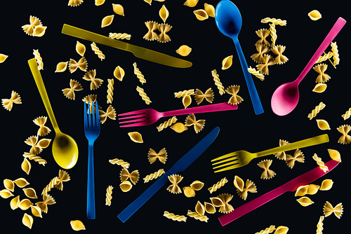 top view of mixed colorful knives, forks and spoons with different kinds of pasta isolated on black