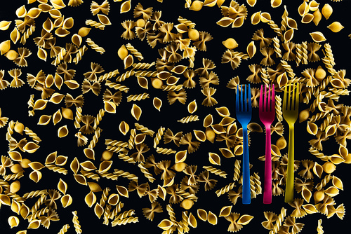 top view of plastic colorful forks on mixed uncooked pasta isolated on black