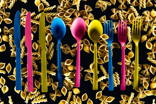 top view of colorful cutlery on different kinds of pasta isolated on black