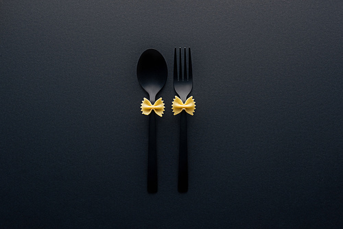 uncooked farfalle pasta on plastic spoon and fork isolated on black