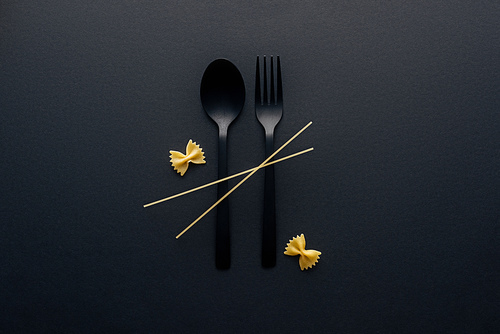 plastic spoon and fork with farfalle pasta and spaghetti on black background