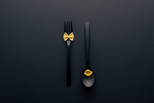 top view of spoon upside down with shell macaroni and fork with farfalle pasta on black background