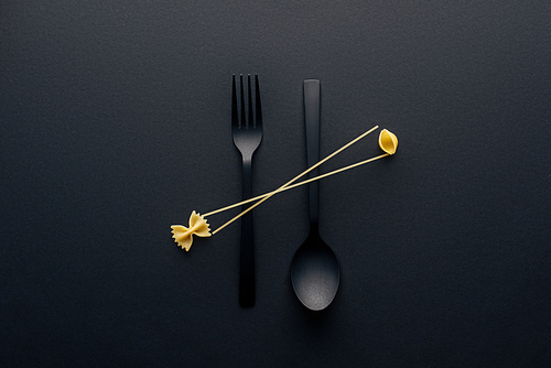 flat lay of spaghetti, farfalle pasta and shell macaroni on spoon upside down and fork on black background