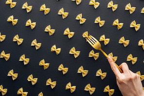 cropped view of woman trying to take farfalle pasta with plastic yellow fork isolated on black