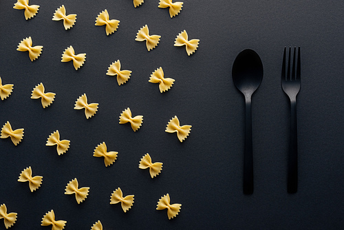 flat lay of farfalle pasta near plastic spoon and fork on black background