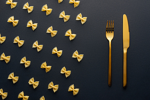 flat lay of farfalle pasta near golden knife and fork on black background