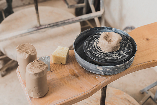 high angle view of wet piece of clay on pottery wheel and sponge on wooden bench in art studio
