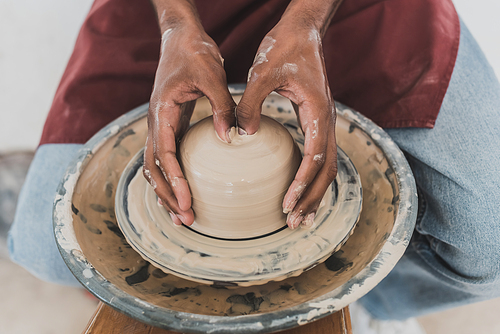 close up view of young african american man modeling wet clay on wheel with hands in pottery