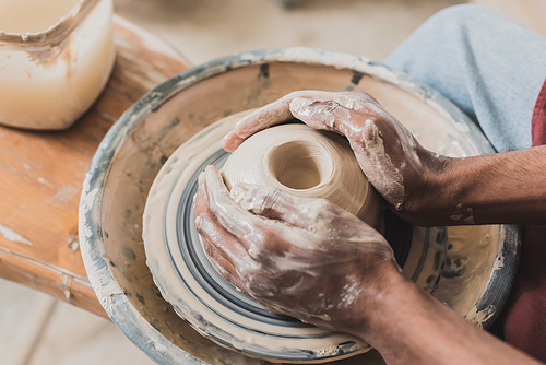 close up view of young african american man modeling wet clay on wheel with hands in pottery
