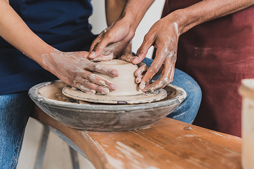 partial view of young african american couple modeling wet clay on wheel with hands in pottery