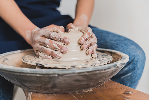 partial view of young african american woman modeling wet clay on wheel with hands in pottery