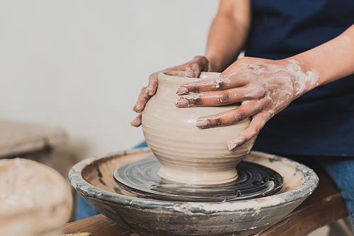 partial view of young african american woman modeling wet clay pot on wheel in pottery