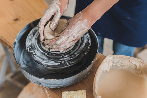 partial view of young african american woman shaping wet clay pot on wheel near sponge and water in plastic box in pottery