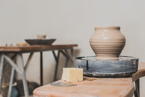 wet clay pot on pottery wheel and sponge on wooden bench in art studio