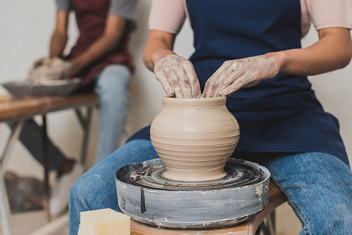 partial view of young african american couple in aprons working with clay pot on wheel in pottery