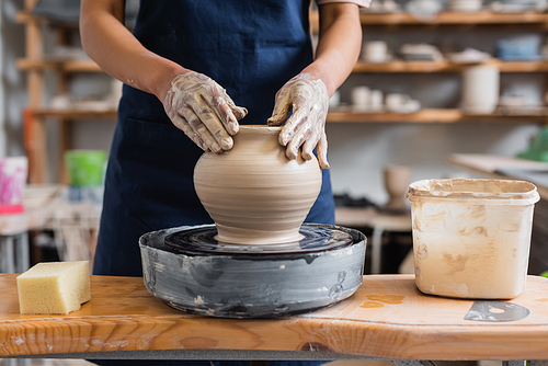 partial view of young african american woman shaping wet clay pot on wheel in pottery