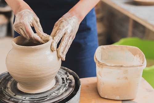 close up view of young african american woman shaping wet clay pot on wheel with hands in pottery
