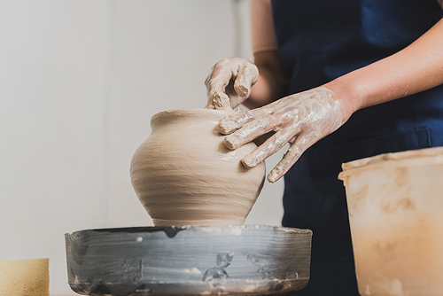 partial view of young african american woman shaping wet clay pot on wheel with hands in pottery