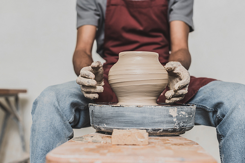 partial view of young african american man sculpting pot on wheel in pottery