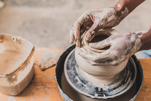 close up view of male african american hands sculpting clay pot on wheel in pottery