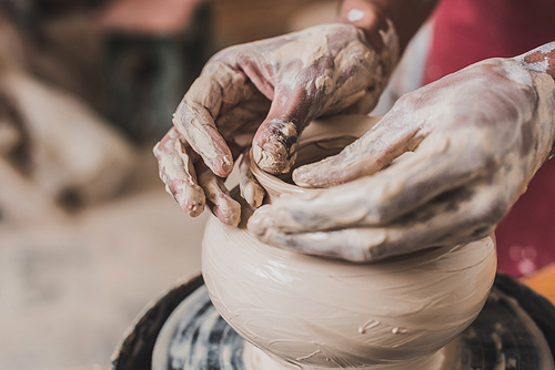 close up view of male african american male hands sculpting clay pot on wheel in pottery