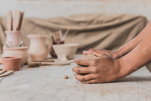 partial view of female african american hands holding clay piece on wooden table in pottery
