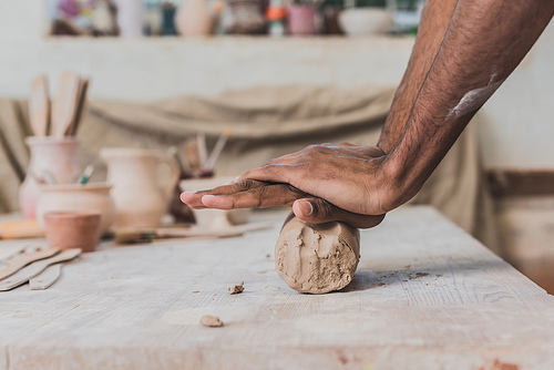 male african american hands working with clay on wooden table in pottery