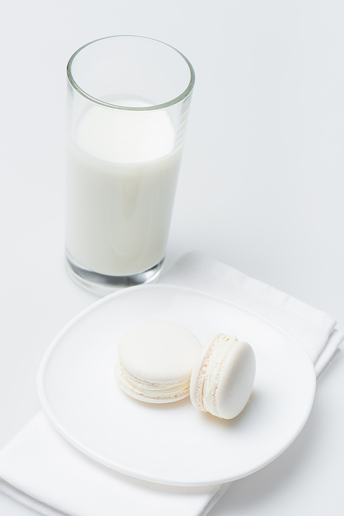 delicious macarons on plate near glass of milk isolated on white