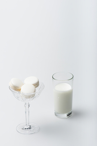 tasty macarons in dessert dish near glass of milk on white