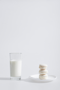 glass of milk near tasty macarons on plate on white