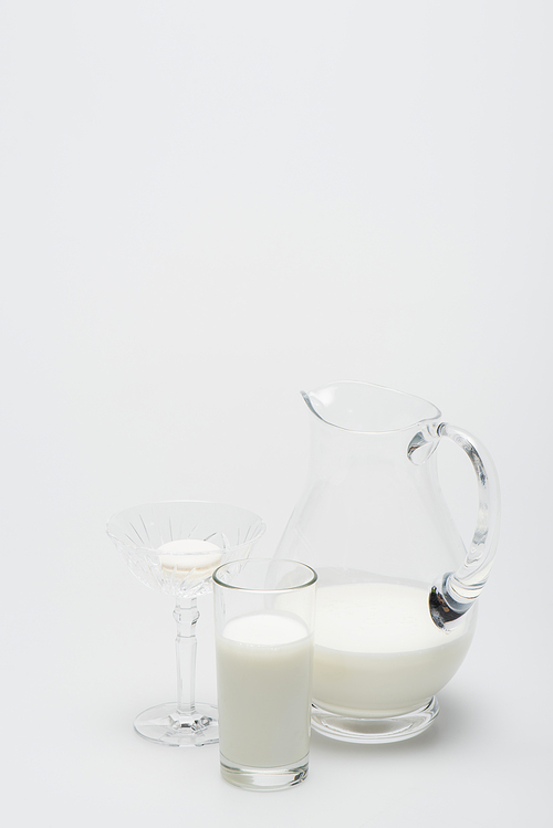 macaron in dessert dish near glass of milk and jug on white