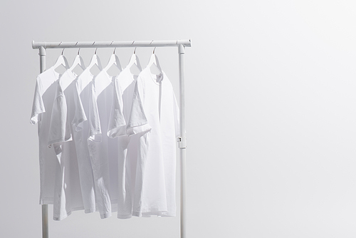 collection of white t-shirts hanging on clothes rack isolated on grey
